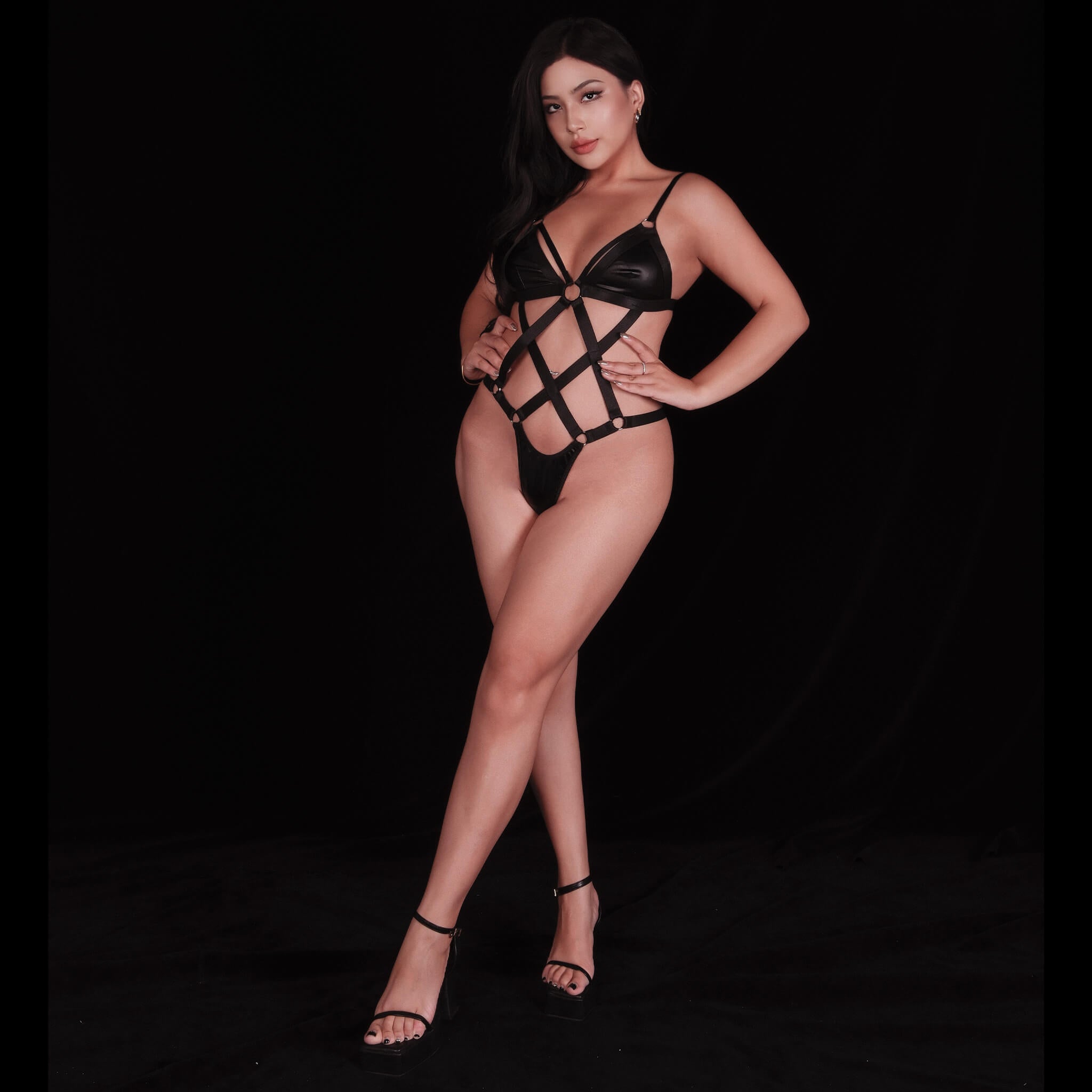 Black strappy leather bodysuit with seductive cutout accents and stylish strap designs, emphasizing curves and creating a confident, provocative look.
